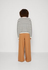 Maglione a righe bianche e nere con scollatura rotonda, abbinato a pantaloni beige a gamba larga. Materiali morbidi e texturizzati con una vestibilità comoda.