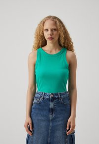 Green ribbed tank top with a round neckline, paired with a blue denim skirt featuring pockets and a button closure.