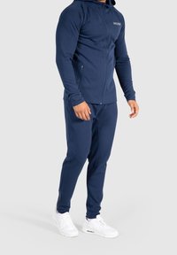 Chándal atlético de la marina con sudadera con cremallera y pantalones jogger, hecho de tela suave, con un diseño ajustado y zapatillas blancas.