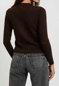 Maglione marrone con un design aderente, maniche lunghe e texture a coste, abbinato a jeans in denim grigio a vita alta con tasche posteriori.