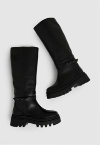 Svarta läderknähöga stövlar med en kraftig sula, prydda med en omlottrem med metalliska detaljer och en slät yta.