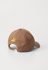 Brown cap with yellow accents and "KING" embroidery. Features a curved brim and adjustable strap at the back. Made of smooth fabric.