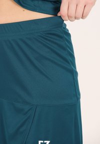 Vihreät urheilushortsit, joissa on sileä ja kevyt kangas. Varustettu leveällä elastisella vyötärönauhalla ja ommelluilla saumoilla kestävyyden lisäämiseksi.