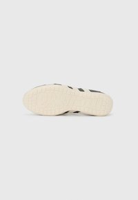 Black sneaker with three stripe design in black, featuring a textured cream-colored sole and embossed logo on the bottom.