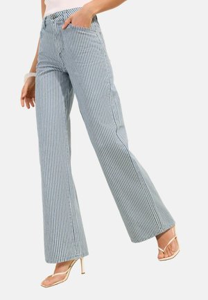 Kvinde iført højtaljede, vidde jeans med smalle lodrette blå og hvide striber, kombineret med beige strop-sandaler med høje hæle.