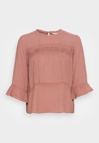 Blouse rose texturée avec de longues manches volantes, présentant des accents en dentelle et un col rond. Elle a une coupe décontractée et fluide avec des détails superposés.