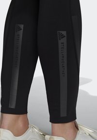 Czarne legginsy sportowe z matowymi i błyszczącymi paskami oraz logo "adidas" i "STELLA McCARTNEY". Wykonane z elastycznego, gładkiego materiału.