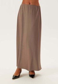 Gonna maxi in un morbido tessuto marrone-grigio. Il design presenta una vita elastica e una forma fluida e morbida. Abbinata a tacchi alti neri.