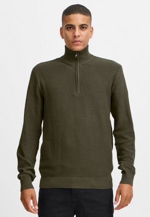Suéter tejido de color verde oliva con un alto cuello y media cremallera. Presenta un patrón texturizado y puños y dobladillo acanalados.