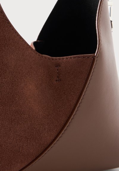 Gros plan d'un sac en cuir marron avec un panneau en daim, une couture surpiquée et un intérieur sombre.