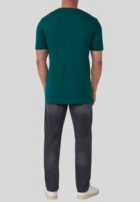 Teal katoenen t-shirt met korte mouwen, ronde hals en een relaxte pasvorm, gecombineerd met donkergrijze jeans en witte sneakers.