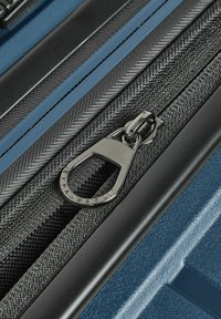 Maleta rígida azul con cremalleras negras, que cuenta con un acento de tela negra texturizada y un tirador de cremallera metálico etiquetado como "Expandable".