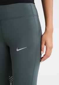 Leggings verdi a vita alta realizzati in tessuto elasticizzato, con logo Nike argentato, texture liscia e cuciture piatte per il massimo comfort.