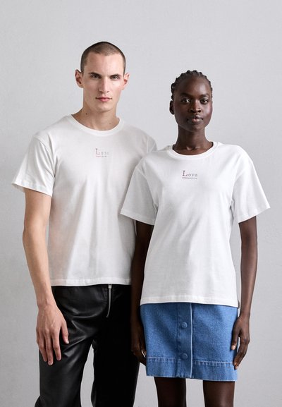 T-shirts en coton blanc avec le texte "Love", associés à une jupe en denim à boutons. Texture douce et design décontracté, adaptés pour un usage quotidien.