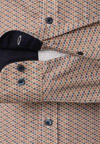 Mankiet i rękaw koszuli z geometrycznym wzorem w kolorach rdzy, niebieskim i beżowym, z czarnymi guzikami i ciemnym podszewką.