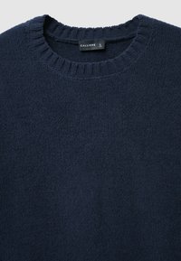 Dunkelblauer Pullover mit einer strukturierten, leicht flauschigen Oberfläche. Verfügt über einen gerippten Rundhalsausschnitt und ein sichtbares Etikett am Kragen.