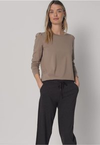 Beiges Langarmshirt mit gerafften Schultern, kombiniert mit dunkelgrauen, mit Kordelzug versehenen Hosen mit Seitentaschen und lockerer Passform.