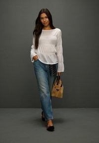 Biely textúrovaný top s dlhým rukávom, modré džínsy s vysokým pásom, čierne baleríny a hnedá kabelka s čiernymi prvkami.