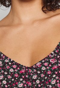 Tissu imprimé floral avec de petites fleurs roses et blanches sur un fond noir. Design à encolure en V avec des détails texturés.