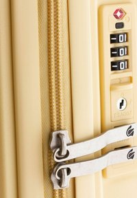 Maleta rígida en beige con un acabado texturizado, cremalleras metálicas dobles y un candado de combinación aprobado por la TSA para mayor seguridad.
