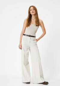 Witte wijde broek met voorplooien en een zwarte riem. De top is een aansluitend beige tanktop. Gladde, lichte stof met een gepolijste afwerking.