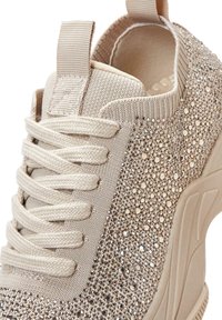 Zapatillas beige con una parte superior de malla texturizada, adornadas con brillantes strass en el lateral, con cordones planos y una tira en la parte trasera.