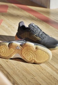 Scarpe sportive nere con tomaia in rete testurizzata, design a pois gialli e suole gommate con motivi a spirale per aderenza e trazione.