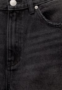 Gros plan d'un jean en denim noir montrant la ceinture avec bouton, passants de ceinture, poche avant et détails des rivets.