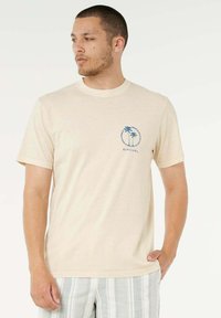 T-shirt in cotone beige con grafica di una palma blu e logo circolare sul lato sinistro del petto. Scollo rotondo e maniche corte.