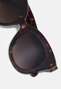 Tortoiseshell sunglasses with dark lenses, featuring a rounded cat-eye design and smooth plastic frames. Notable for subtle color variations.