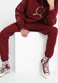 Felpa con cappuccio bordeaux con logo dorato e pantaloni abbinati, abbinati a scarpe alte a quadri con lacci bianchi e suole in gomma.