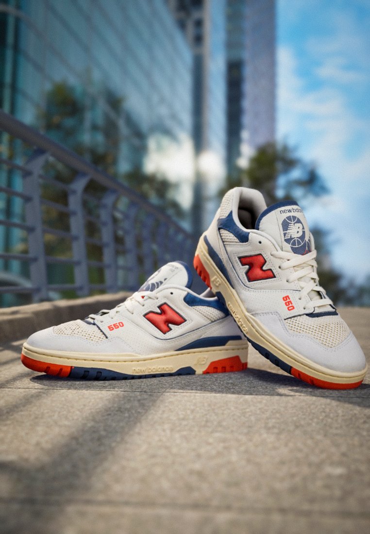 Weiße und graue Sneakers mit roten und blauen Akzenten. Sie verfügen über ein Mesh-Material, einen gepolsterten Schaft und eine Gummisohle mit einem strukturierten Muster.