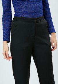 Zwarte broek met een gladde textuur, voorzien van een verborgen rits aan de voorkant en een slim-fit ontwerp. Gekoeld met een blauwe kanten top met lange mouwen.
