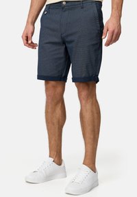 Pantalones cortos azul marino con un patrón texturizado, con puños enrollados y cierre de botón, combinados con zapatillas blancas.