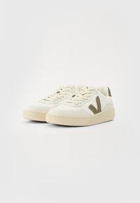 White sneakers with light beige accents, featuring a textured design, round toe, flat laces, and a prominent 'V' logo in dark beige.