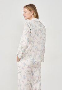 Conjunto de pijama ligero en crema con un patrón divertido de gatos y cintas en azul pastel y rosa. Tejido suave con un corte holgado.