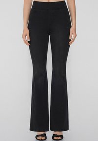 Pantalones acampanados de mezclilla negra con una textura suave, que presentan una cintura alta, bolsillos frontales y detalles de costura.