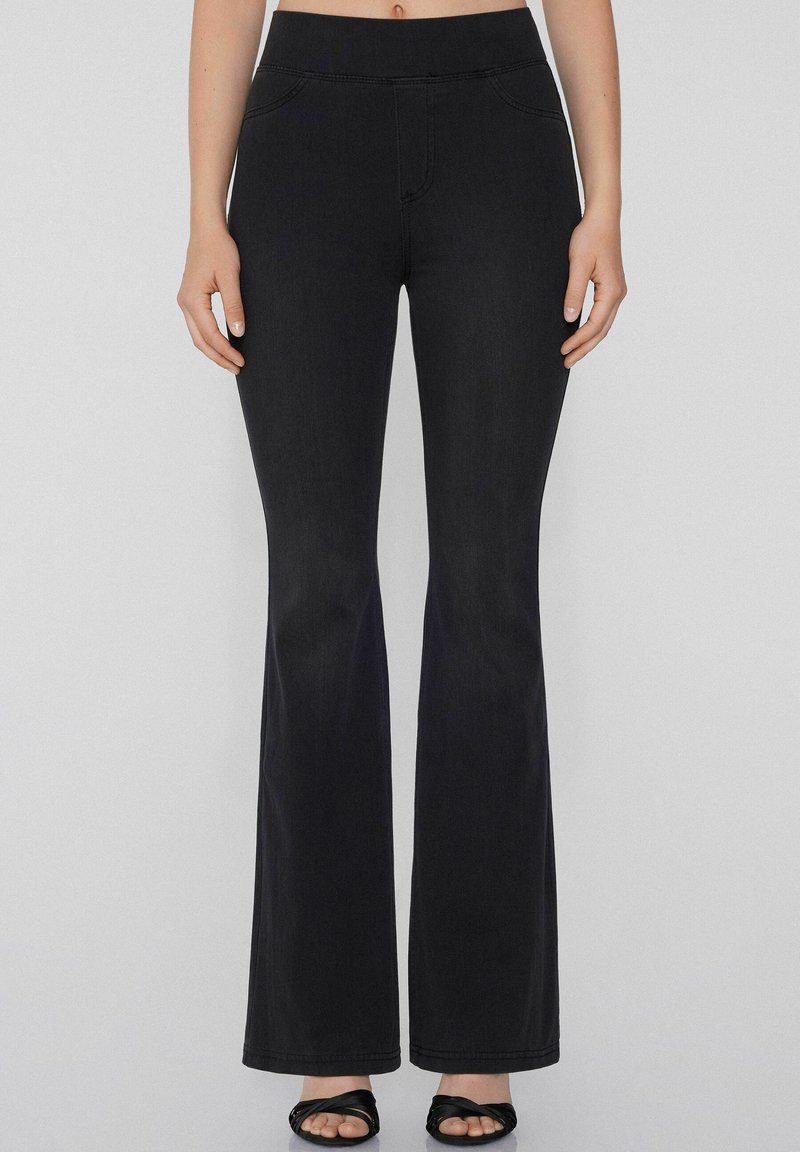 Pantalones acampanados de mezclilla negra con una textura suave, que presentan una cintura alta, bolsillos frontales y detalles de costura.