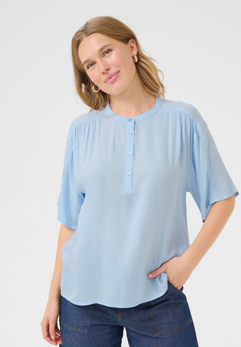 Blusa a maniche corte azzurro chiaro realizzata in tessuto morbido, con scollatura rotonda e chiusura a bottoni frontale. Vestibilità casual con una caduta morbida.