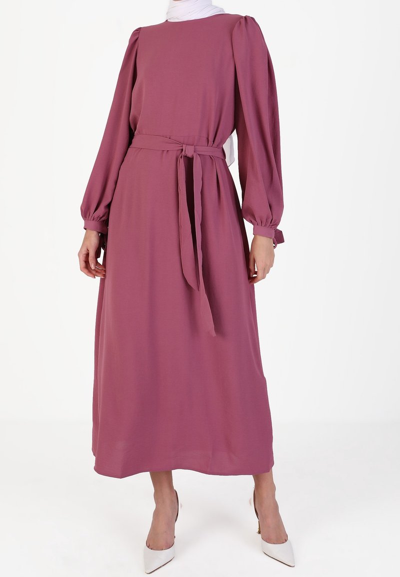 Robe mauve à manches longues avec encolure ronde, taille cintrée et ceinture assortie. Tissu lisse et coupe fluide, se terminant au milieu du mollet.