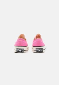 Różowe płócienne trampki o niskim kroju. Posiadają gumowe podeszwy, kontrastowe czarne akcenty oraz branding "Converse All Star" na pięcie.