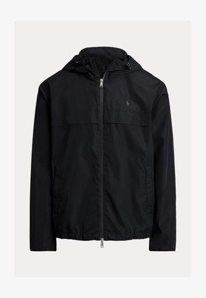 Čierna vetrovka s kapucňou, s predným zipsovým zapínaním, dvoma bočnými vreckami a diskrétnym logom na hrudi. Hladká, ľahká tkanina.