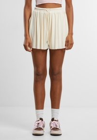 Krämfärgade shorts med elastiskt midjeband, dragsko-detall och lös passform, i kombination med bruna sneakers och vita ankelsockor.