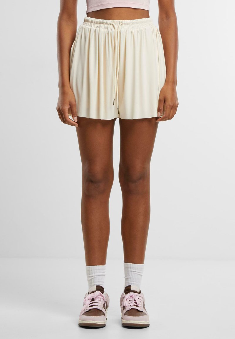 Krämfärgade shorts med elastiskt midjeband, dragsko-detall och lös passform, i kombination med bruna sneakers och vita ankelsockor.
