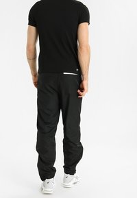 Maglietta nera a maniche corte abbinata a pantaloni jogger neri e leggeri con polsini elasticizzati e un sottile accento riflettente vicino alla tasca.