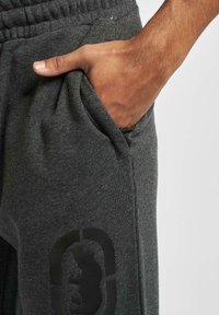 Fleece joggers i mørkegrå med en blød tekstur, elastisk talje, sidelommer og et diskret sort logo-design på låret.