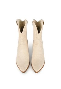 Botines de ante beige con punteras afiladas, costuras decorativas y cremalleras laterales; textura suave, características de diseño mínimas.