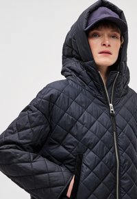 Čierna prešívaná bunda s vysokým golierom, so zipsovým zapínaním a bočnými vreckami. Hladký, lesklý povrch zvyšuje teplo.