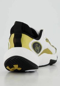 Scarpa sportiva bianca con accenti neri e gialli, caratterizzata da una suola testurizzata, tomaia in mesh e un logo prominente sul tallone.