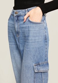 Jasnoniebieskie dżinsowe spodnie cargo z bocznymi kieszeniami, wysokim stanem i luźnym krojem. Materiał ma gładką strukturę z delikatnym wyblaknięciem.